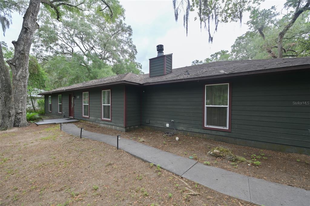 A single-story house with dark green horizontal siding and a chimney stands among trees — 7616 SW 10TH AVENUE, GAINESVILLE, FL