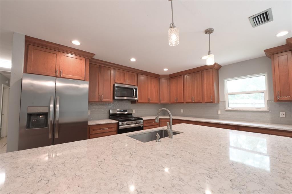 A kitchen features wood cabinets, stainless steel appliances, and a large quartz-topped island — 7616 SW 10TH AVENUE, GAINESVILLE, FL