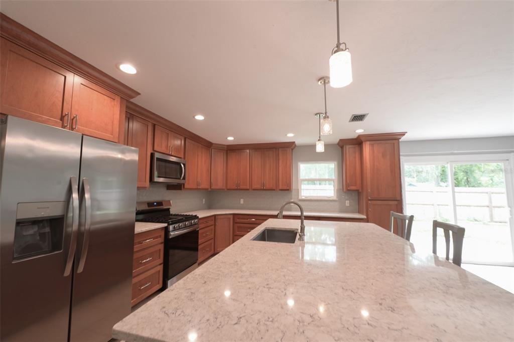 A kitchen features wood cabinets, stainless steel appliances, a large island, and quartz countertops — 7616 SW 10TH AVENUE, GAINESVILLE, FL