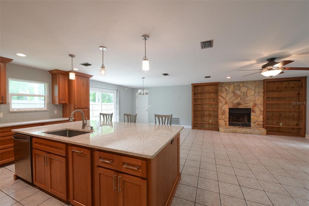 A kitchen with a granite island and wood cabinets opens to a living room with a fireplace — 7616 SW 10TH AVENUE, GAINESVILLE, FL