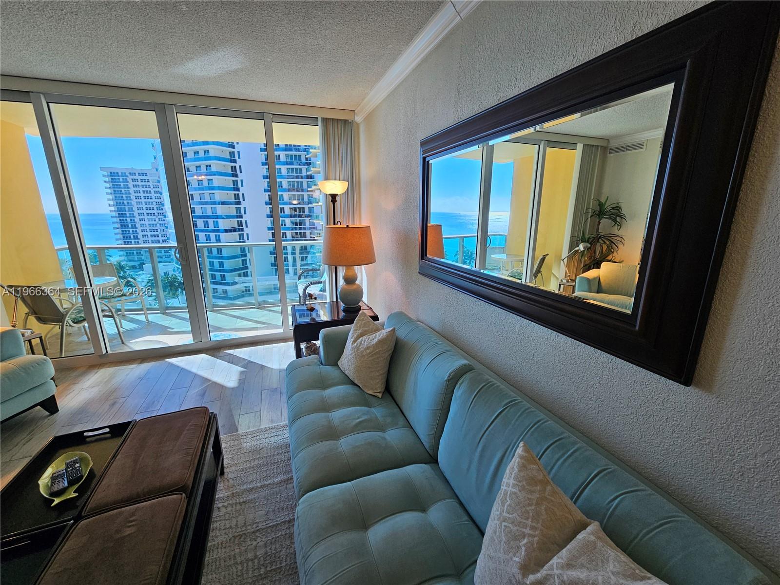 A living room features a light blue sofa, a large wall mirror, and a balcony view — 2501 S Ocean Dr, Hollywood FL 33019, HOLLYWOOD, FL