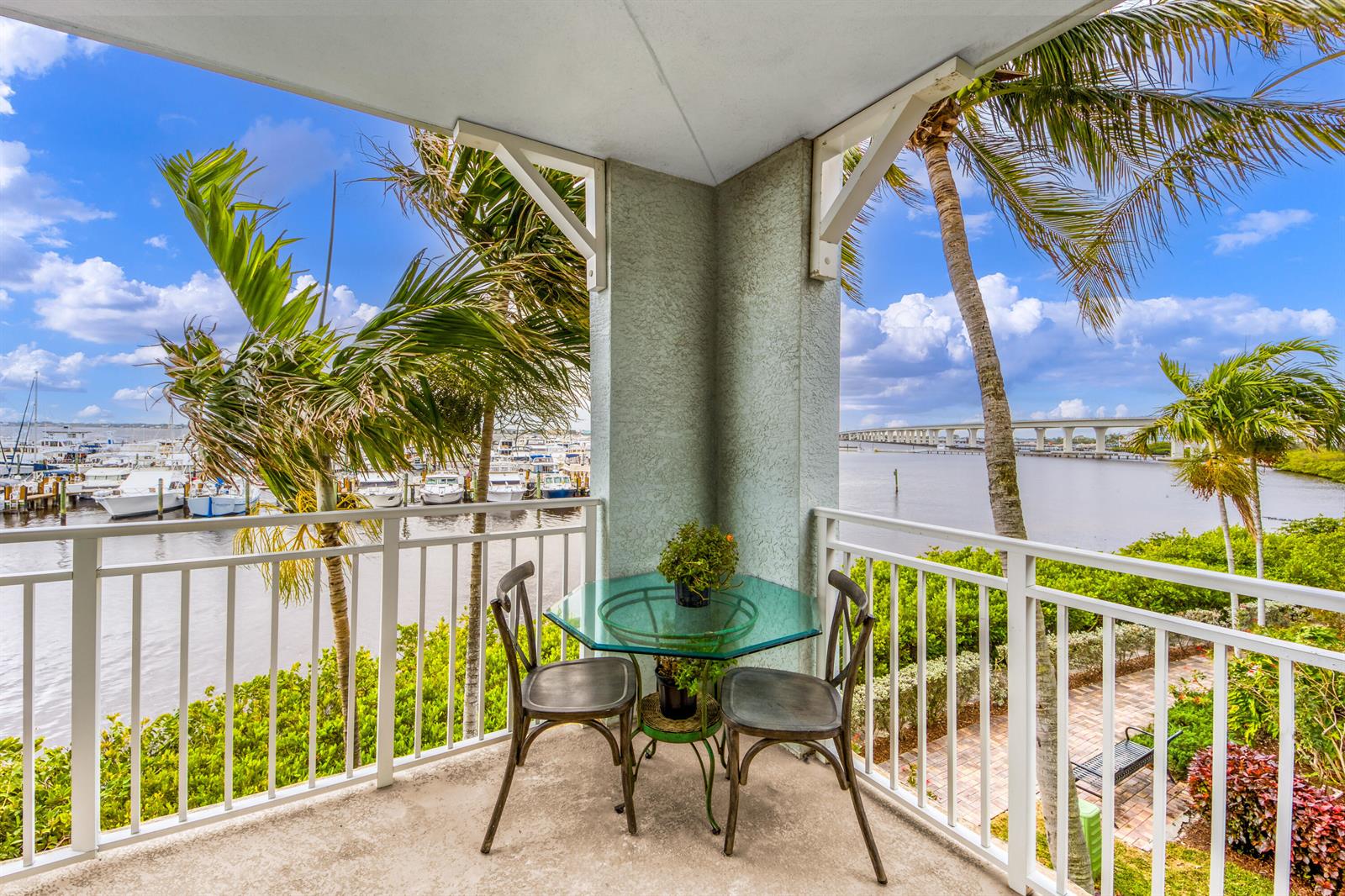 A balcony with a glass table and two chairs overlooks a marina and a bridge — 875 NW Flagler Avenue # 203, Stuart FL 34994, STUART, FL