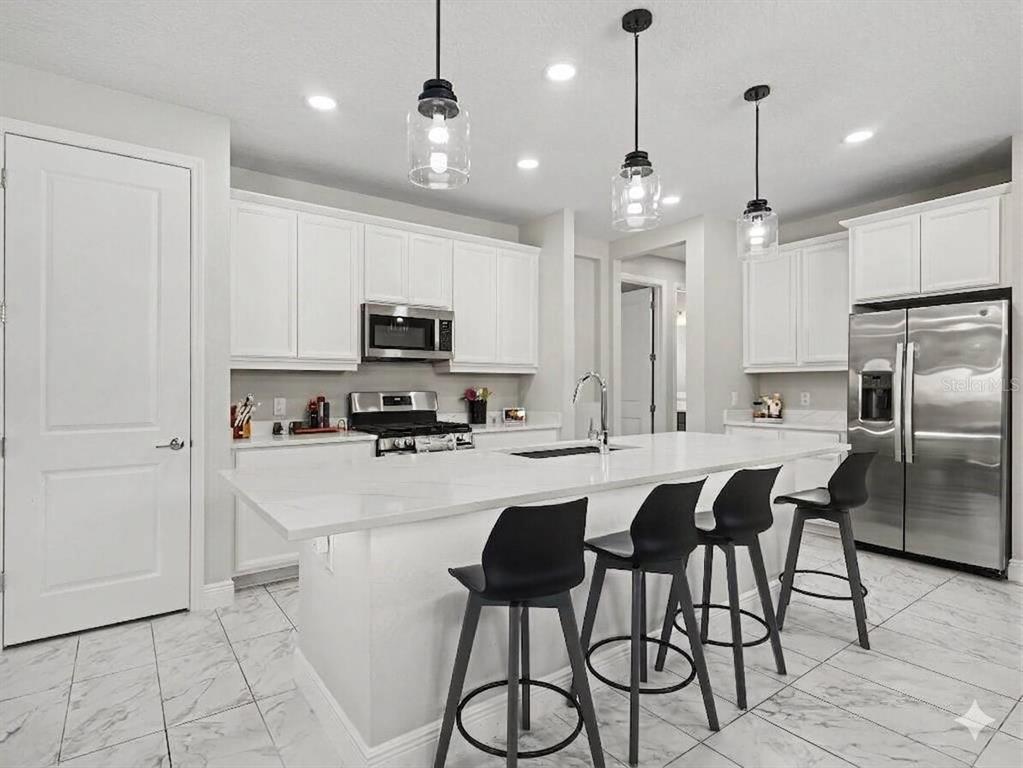 A modern kitchen features white cabinetry, a marble-topped island, stainless steel appliances, and tile flooring — 8144 STERNWAY ROAD, SARASOTA, FL