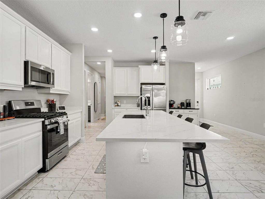 A modern kitchen features white cabinetry, a large quartz island, and four black bar stools — 8144 STERNWAY ROAD, SARASOTA, FL