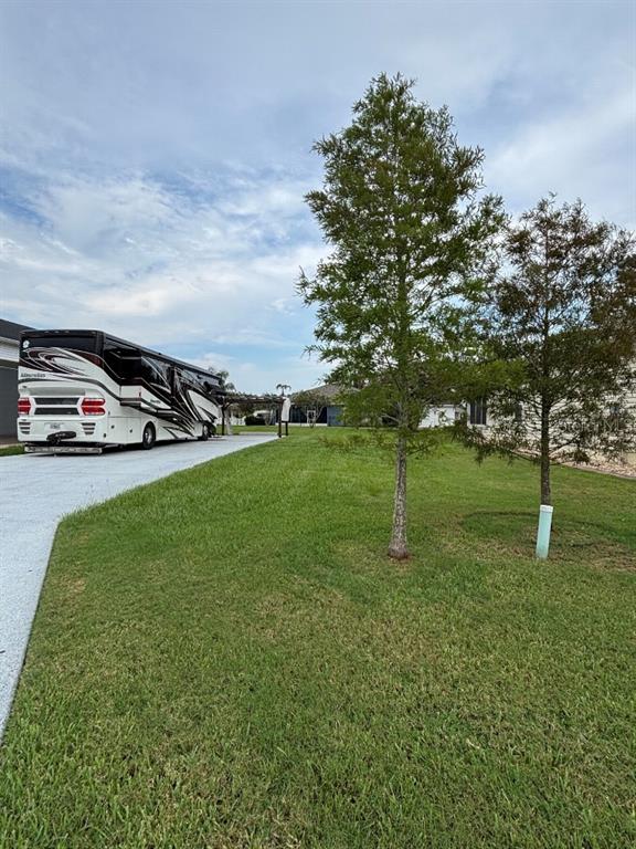 A large recreational vehicle is parked on a concrete driveway next to two young trees — 1098 MOTORCOACH DRIVE, POLK CITY, FL