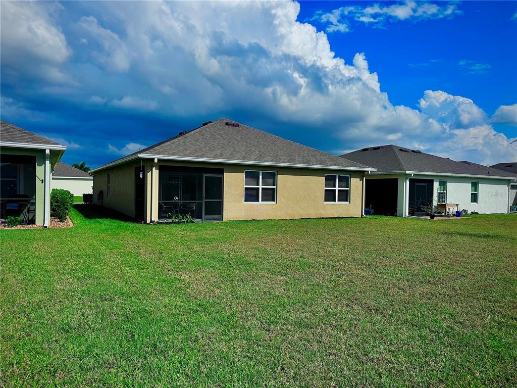 The rear exterior of a tan house with a screened-in patio and a grassy yard — 4077 MANATEE LANE, PUNTA GORDA, FL