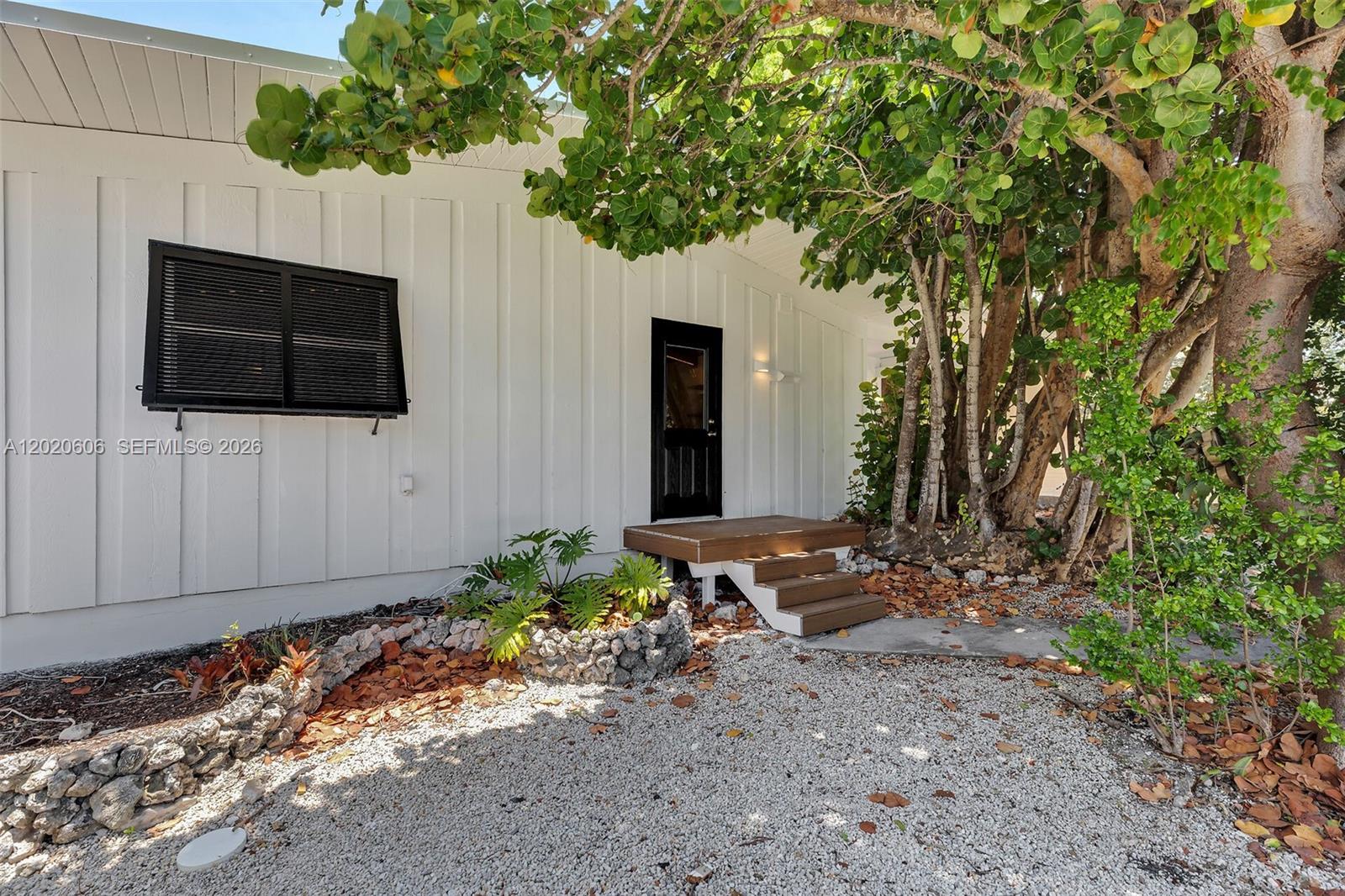 A white house exterior features a black door, a black window shutter, and wooden steps — 178 Coral Ave, Tavernier FL 33070, TAVERNIER, FL