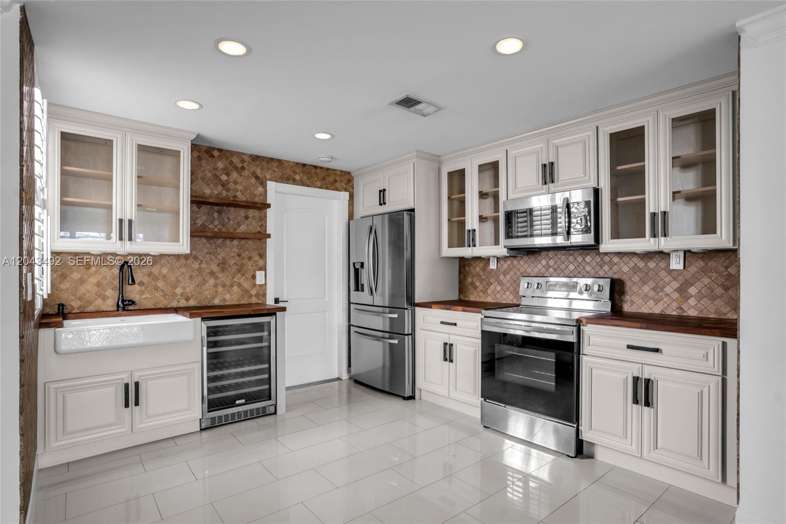 A kitchen features white cabinetry, stainless steel appliances, a farmhouse sink, and brown tile backsplash — 1231 Sorrento Dr # 1231, Weston FL 33326, WESTON, FL