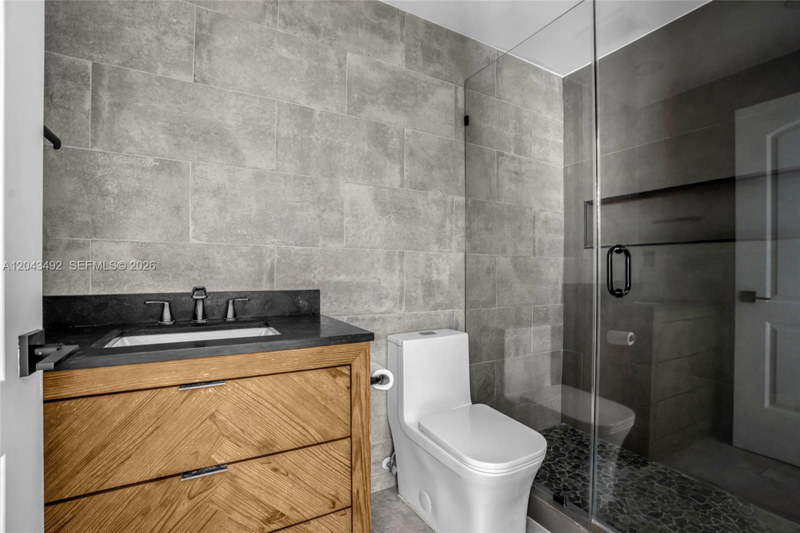 A modern bathroom features a wood vanity, black countertop, white toilet, and a glass-enclosed shower — 1231 Sorrento Dr # 1231, Weston FL 33326, WESTON, FL