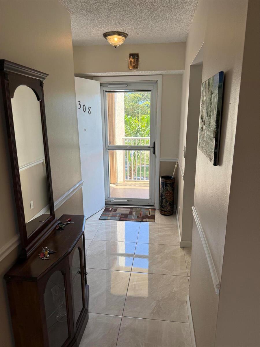 A tiled entryway features a mirror, a console table, and a door leading to a balcony — 1024 SE 5th Avenue # 308, Dania Beach FL 33004, DANIA BEACH, FL