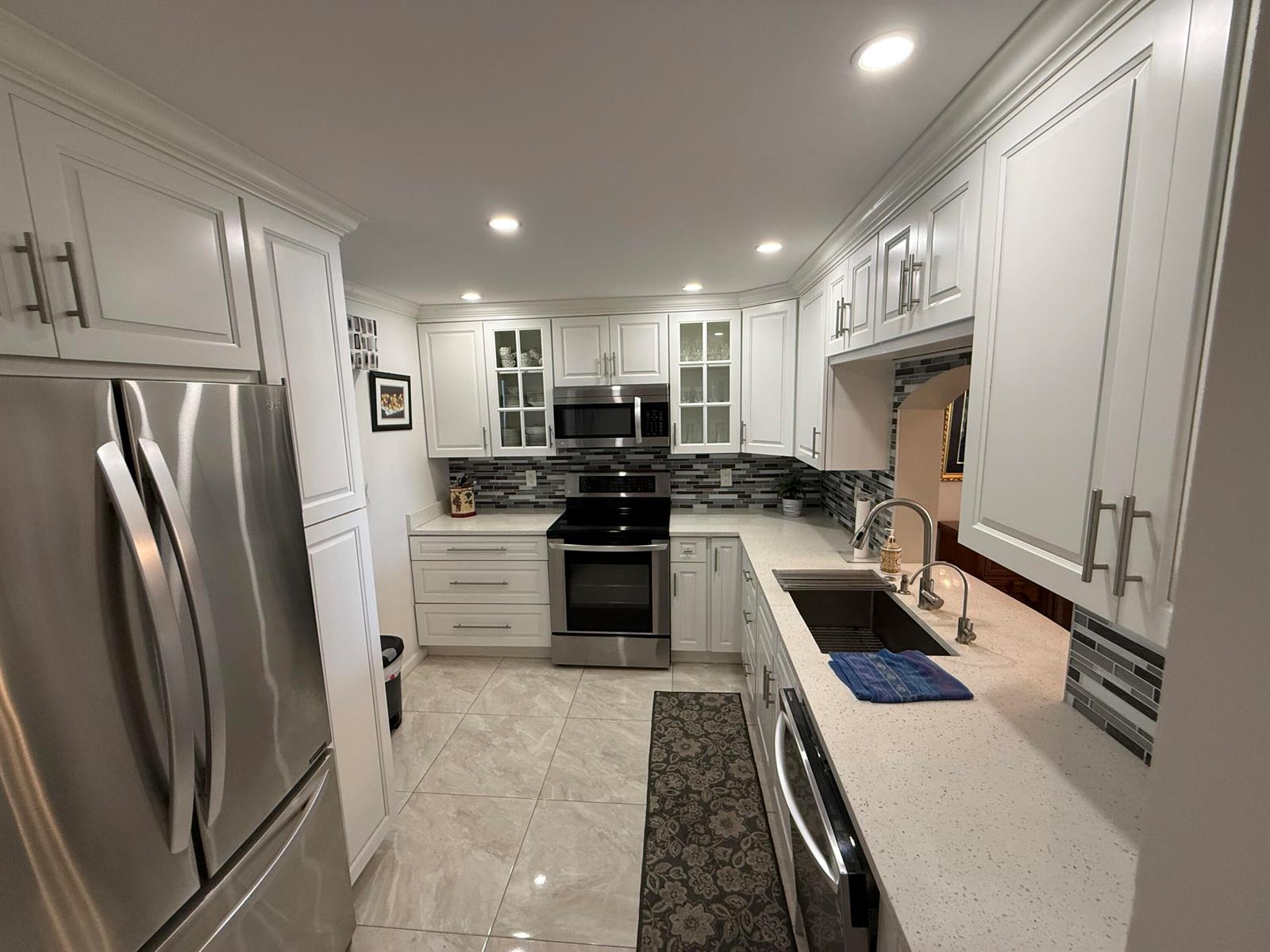 A kitchen features white cabinets, stainless steel appliances, quartz countertops, and a gray tile backsplash — 1024 SE 5th Avenue # 308, Dania Beach FL 33004, DANIA BEACH, FL