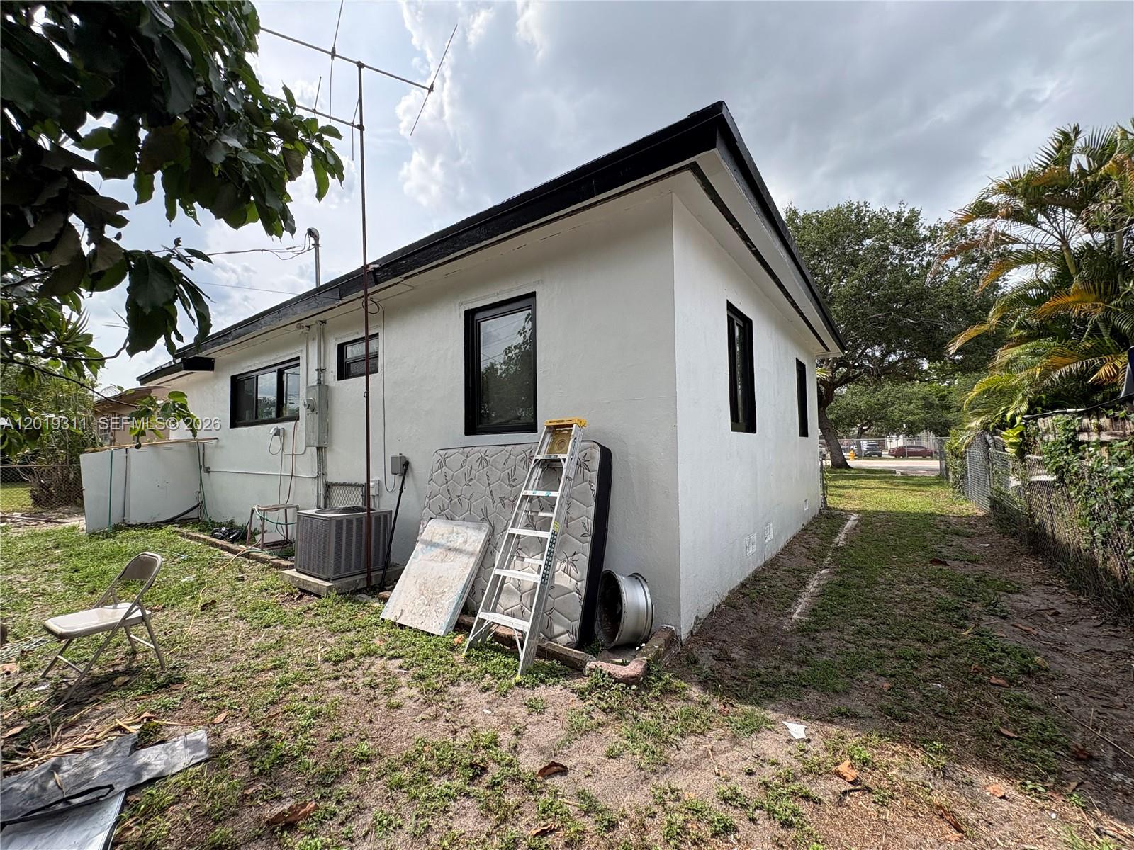 The exterior of a white house features black window frames, a ladder, and a mattress — 1250 NW 131st St, North Miami FL 33167, NORTH MIAMI, FL