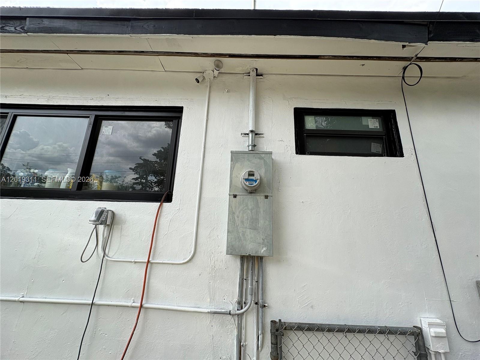 An exterior view of a white wall featuring an electrical meter, conduit, and two windows — 1250 NW 131st St, North Miami FL 33167, NORTH MIAMI, FL