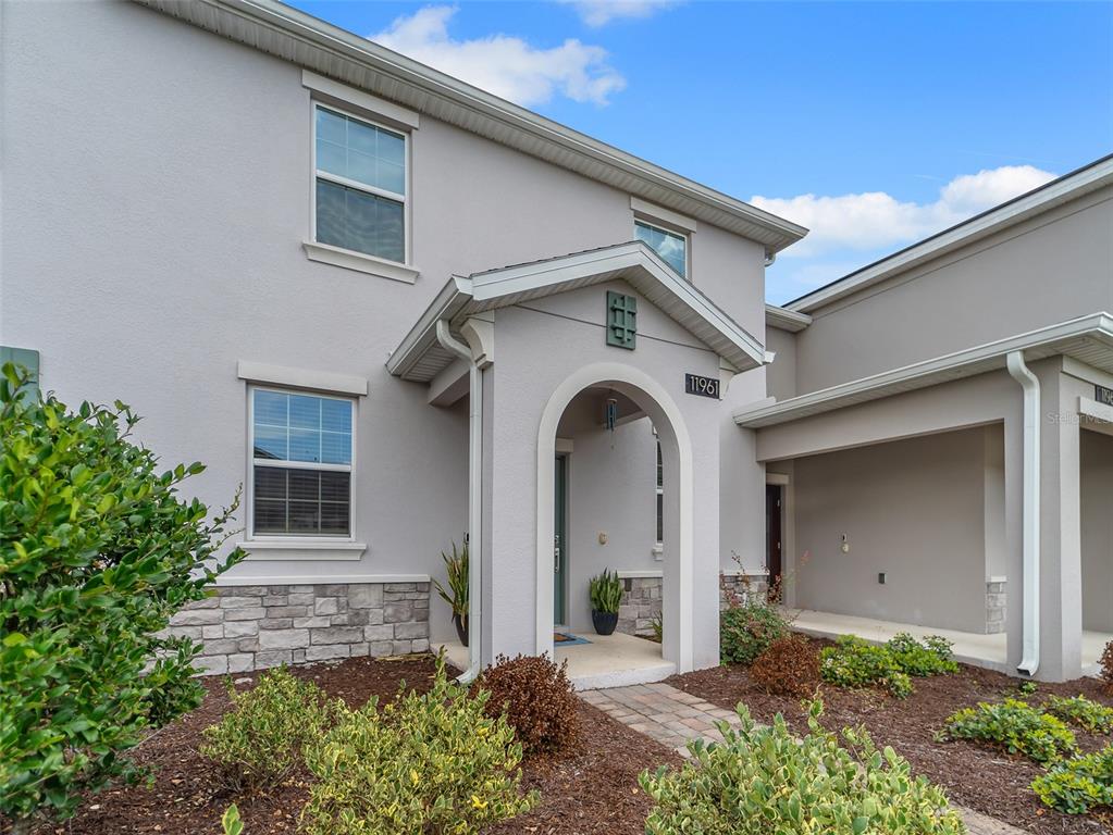 A two-story house exterior features light gray stucco, stone accents, and a covered entryway — 11961 BOLDFACE DRIVE, ORLANDO, FL