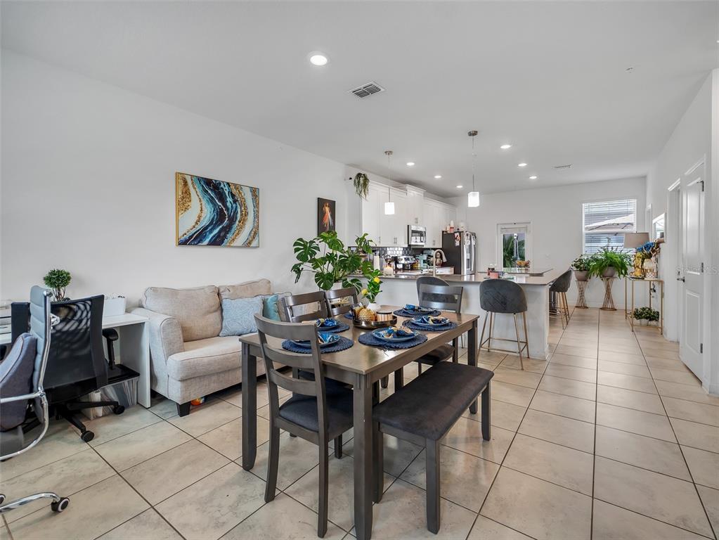 An open-concept dining area and kitchen featuring tile flooring, a wooden table, and white cabinetry — 11961 BOLDFACE DRIVE, ORLANDO, FL