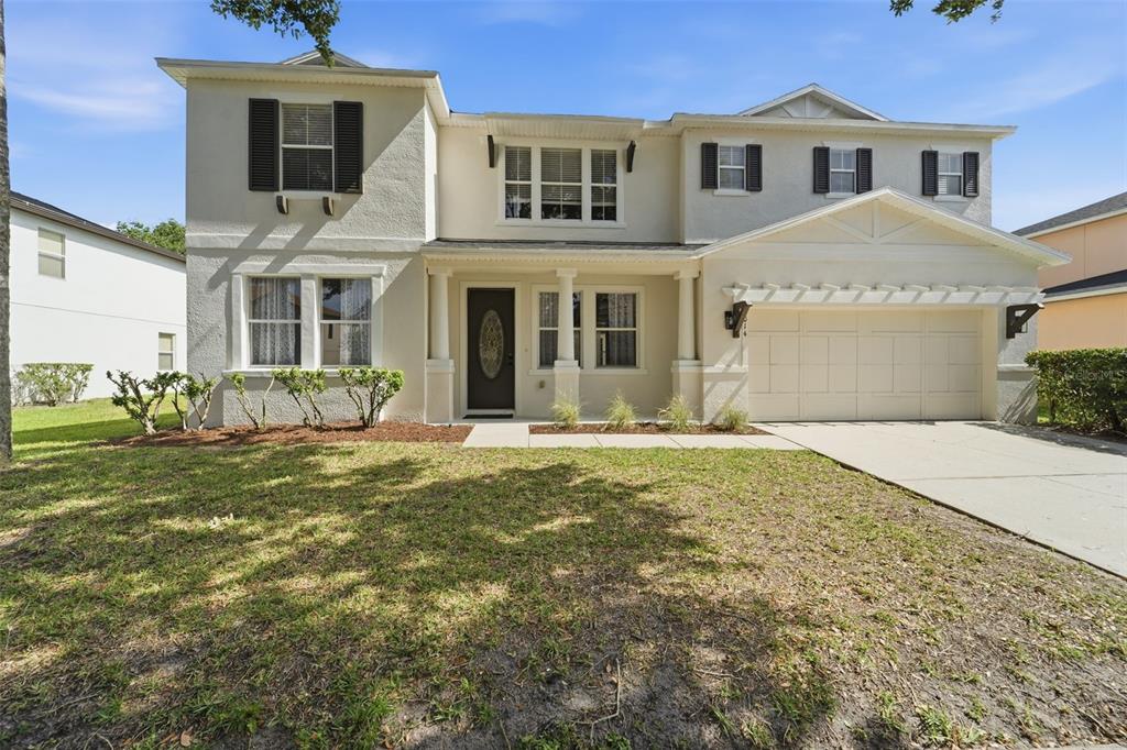 A two-story suburban house with a beige stucco exterior, a front porch, and a garage — 10143 MALPAS POINT, ORLANDO, FL