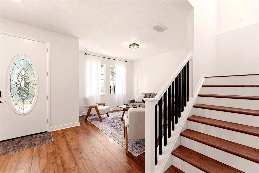 A foyer with wood flooring leads to a living area and a staircase with railings — 10143 MALPAS POINT, ORLANDO, FL