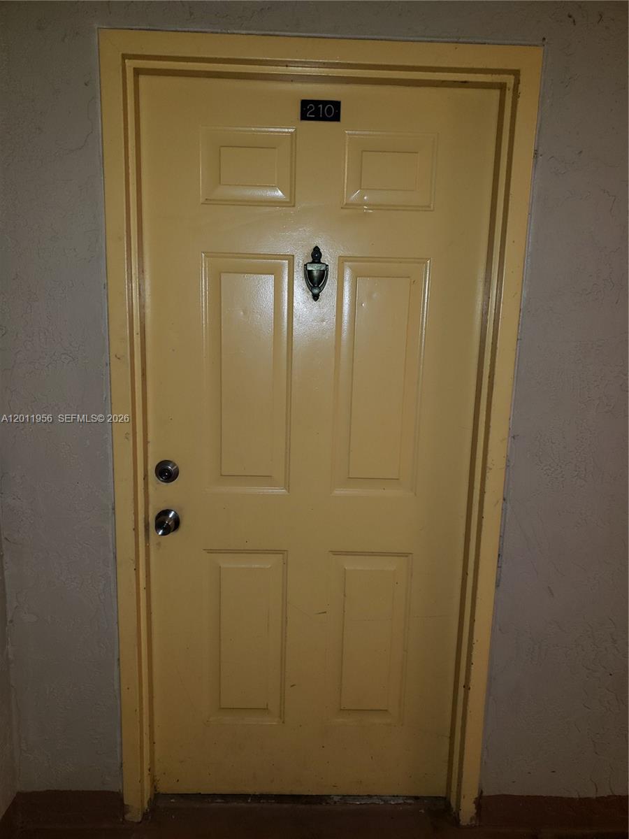 A yellow apartment door with a peephole, knocker, and the number 210 — 15241 SW 80th St # 201, Miami FL 33193, MIAMI, FL