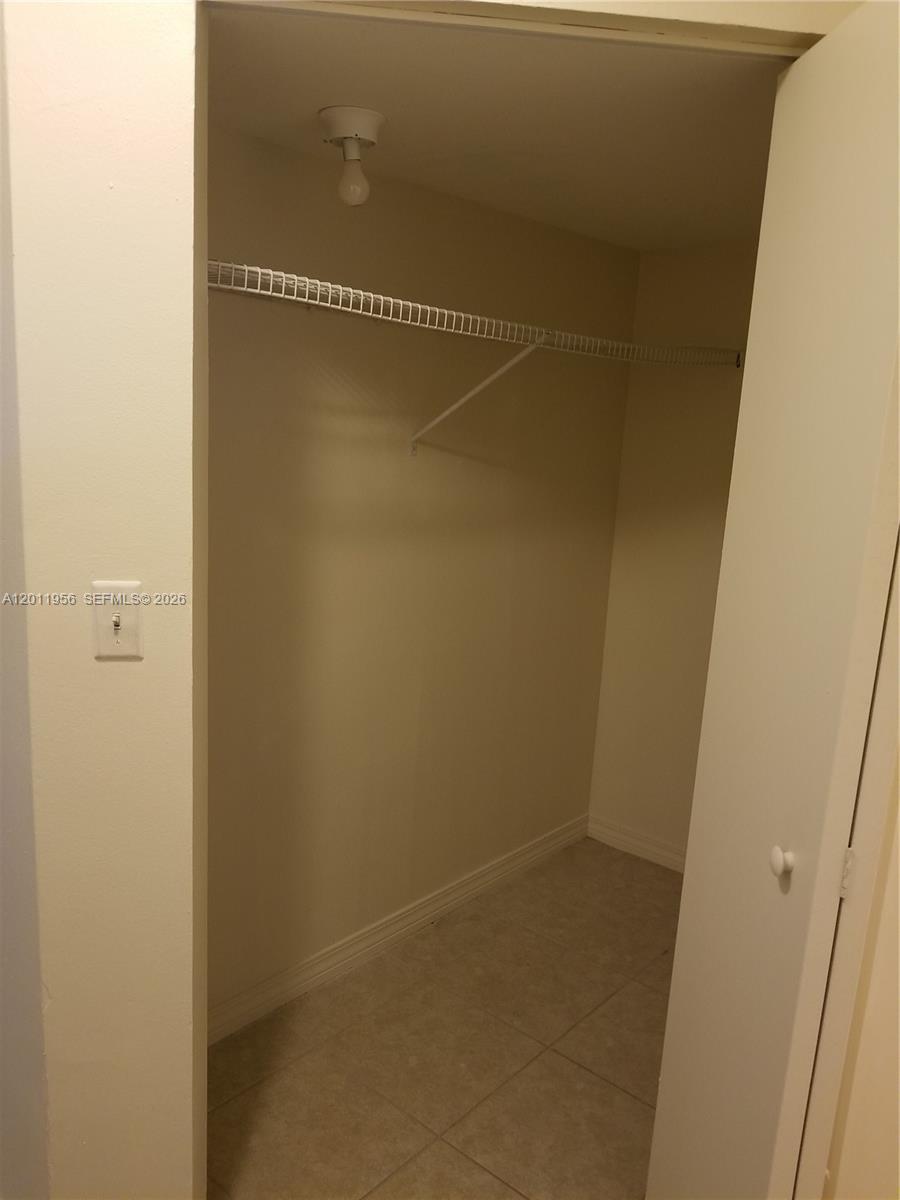 This walk-in closet features a white wire shelf, tile flooring, and a light fixture — 15241 SW 80th St # 201, Miami FL 33193, MIAMI, FL