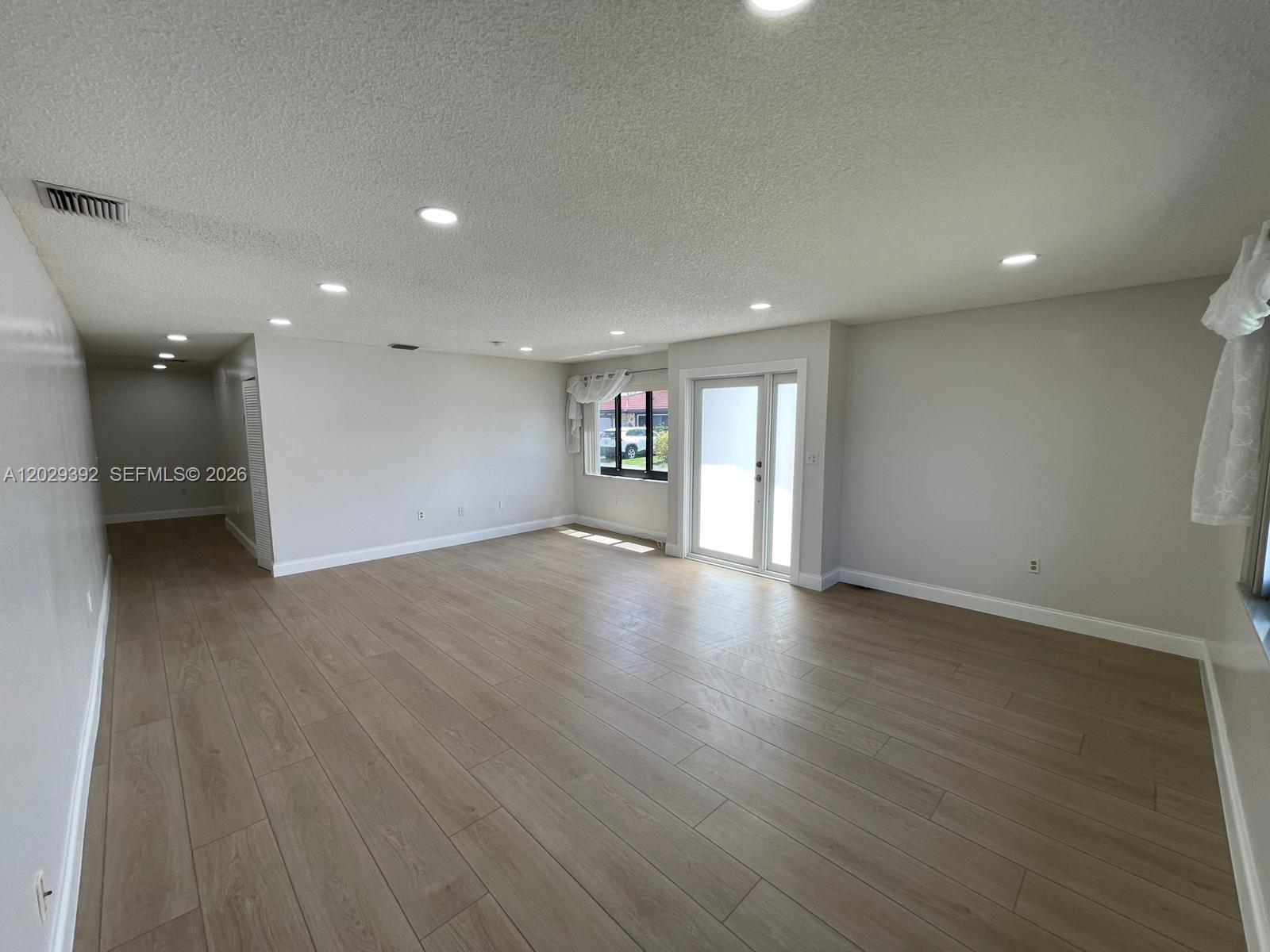 A spacious living room features light wood-look flooring, recessed lighting, and a glass sliding door — 1727 SW 136th Pl, Miami FL 33175, MIAMI, FL
