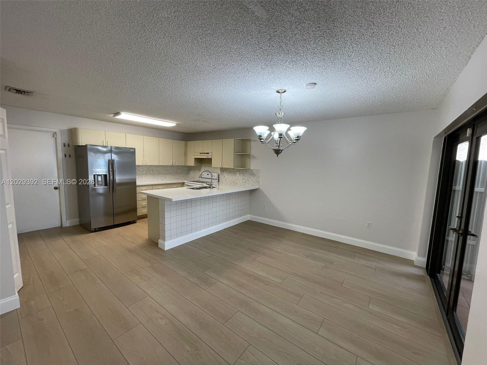 A kitchen with light-colored cabinets, stainless steel appliances, and a breakfast bar opens to a dining area — 1727 SW 136th Pl, Miami FL 33175, MIAMI, FL
