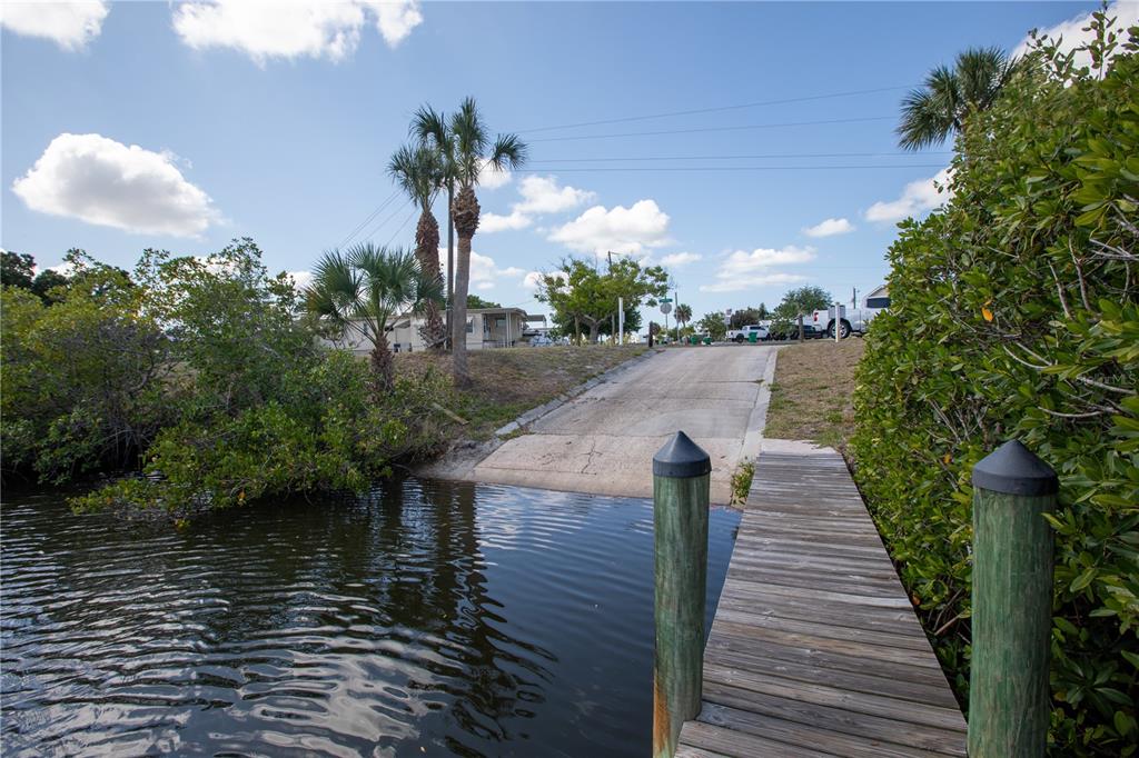 A concrete boat ramp leads from the water to a grassy area with palm trees — 2465 HERON DRIVE, ENGLEWOOD, FL