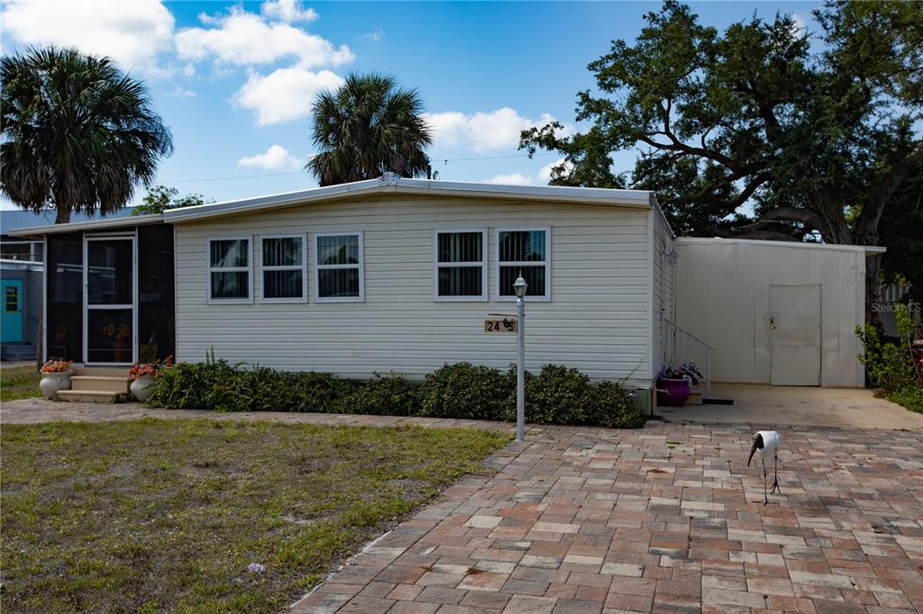 A single-story mobile home with beige siding, a screened porch, and a paved driveway — 2465 HERON DRIVE, ENGLEWOOD, FL