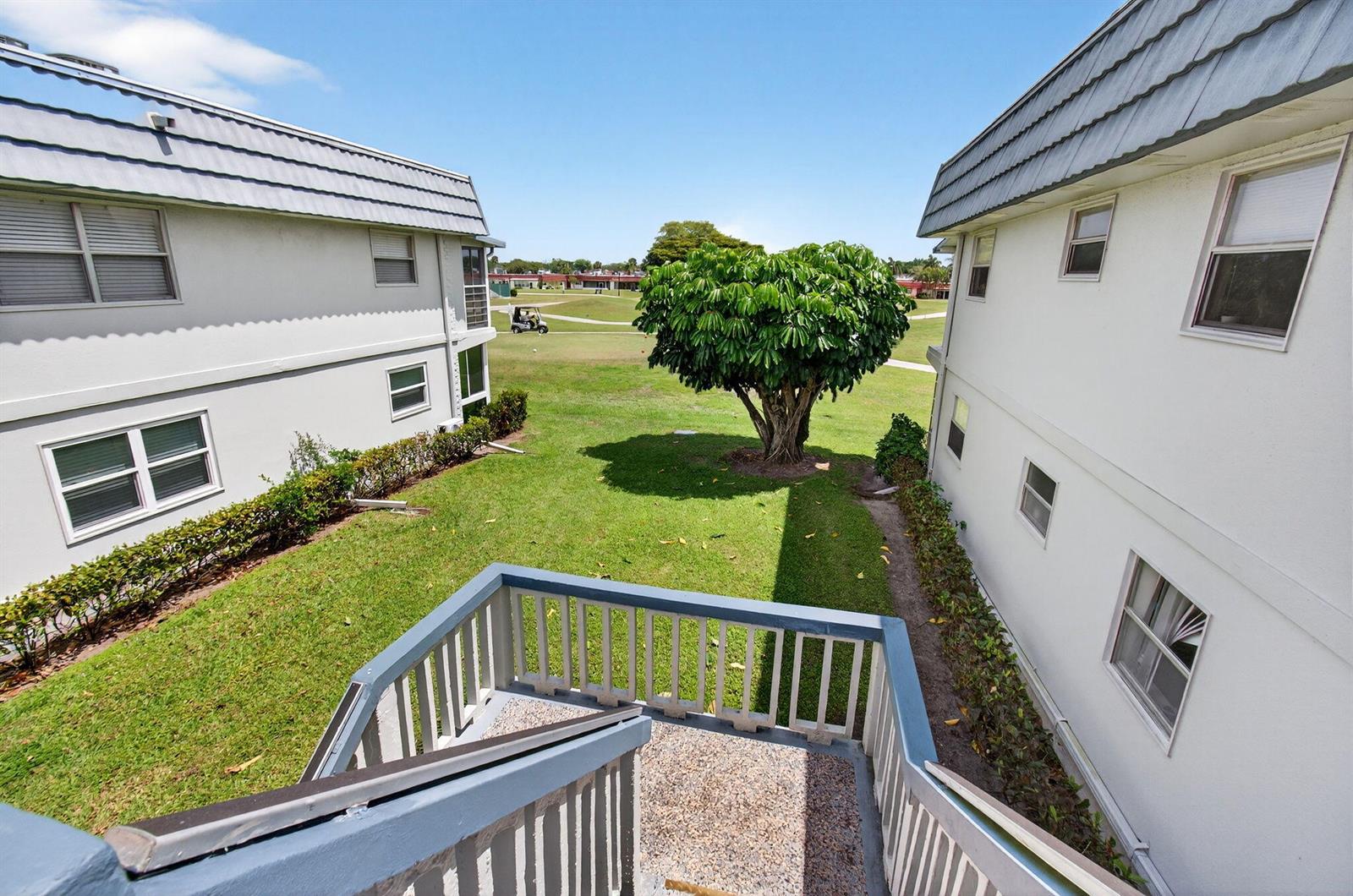 An elevated view from a staircase looking out at a grassy courtyard between two buildings — 186 Tuscany C, Delray Beach FL 33446, DELRAY BEACH, FL