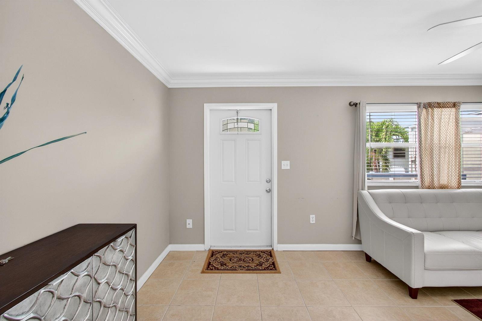 A living room with beige walls, tile flooring, a white front door, and a sofa — 186 Tuscany C, Delray Beach FL 33446, DELRAY BEACH, FL