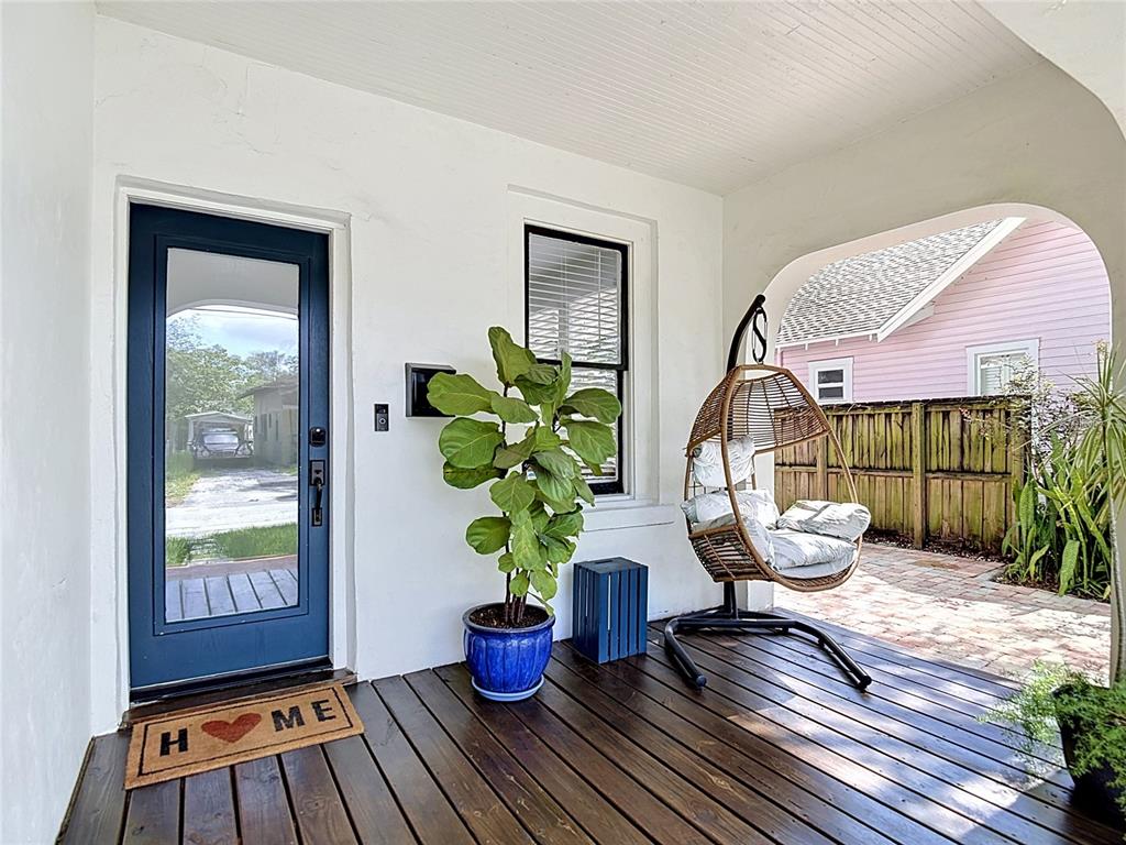 A covered front porch features a dark wood floor, a blue door, and a hanging chair — 105 W ELM STREET, TAMPA, FL