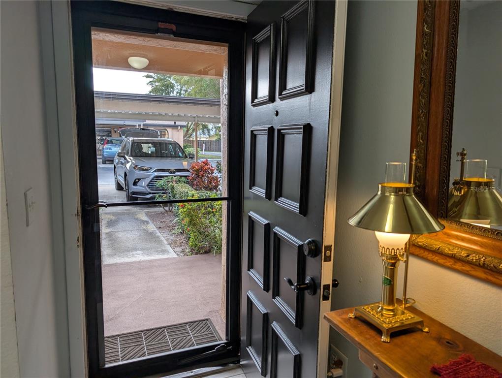 An open black front door reveals a view of a driveway with a parked car — 2808 60TH AVENUE W UNIT 1702, BRADENTON, FL