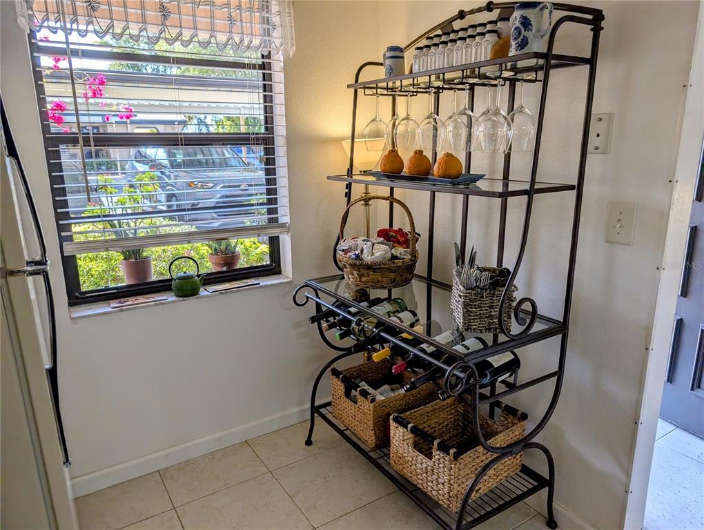 A metal baker's rack with wine storage stands beside a window in a tiled room — 2808 60TH AVENUE W UNIT 1702, BRADENTON, FL