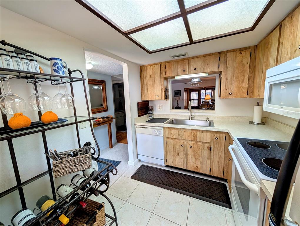 A kitchen features light wood cabinets, a pass-through window, and a metal wine rack — 2808 60TH AVENUE W UNIT 1702, BRADENTON, FL