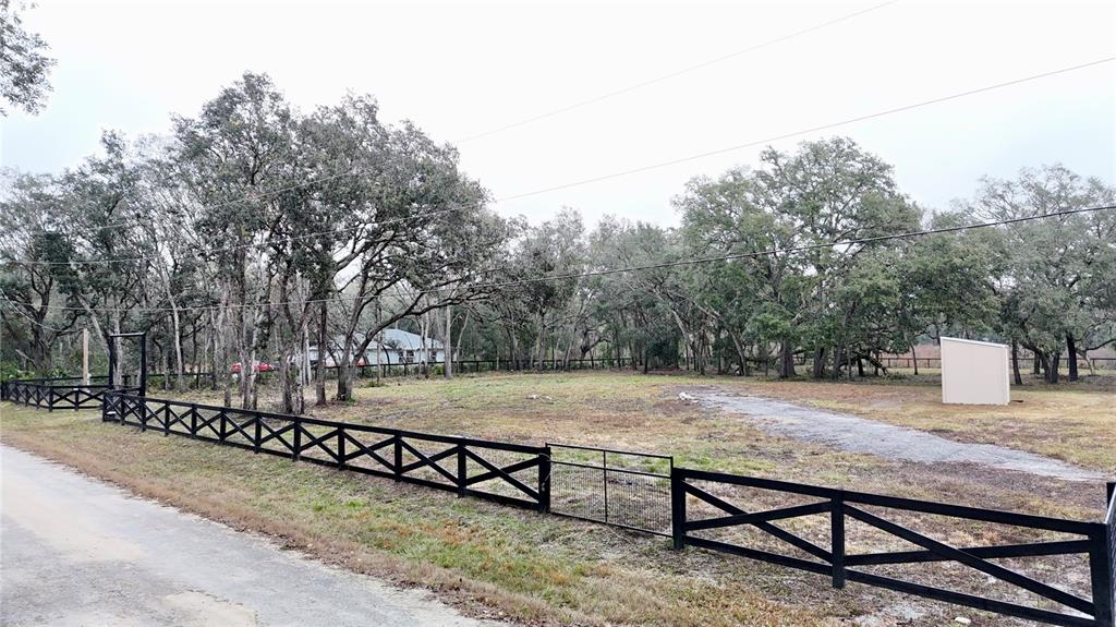 A fenced, grassy lot with mature trees and a small shed under an overcast sky — 7414 ANTIETAM DRIVE, WEBSTER, FL