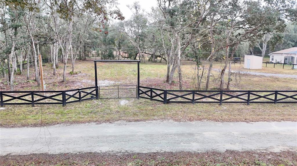 A black wooden fence with a gate encloses a wooded lot next to a house — 7414 ANTIETAM DRIVE, WEBSTER, FL