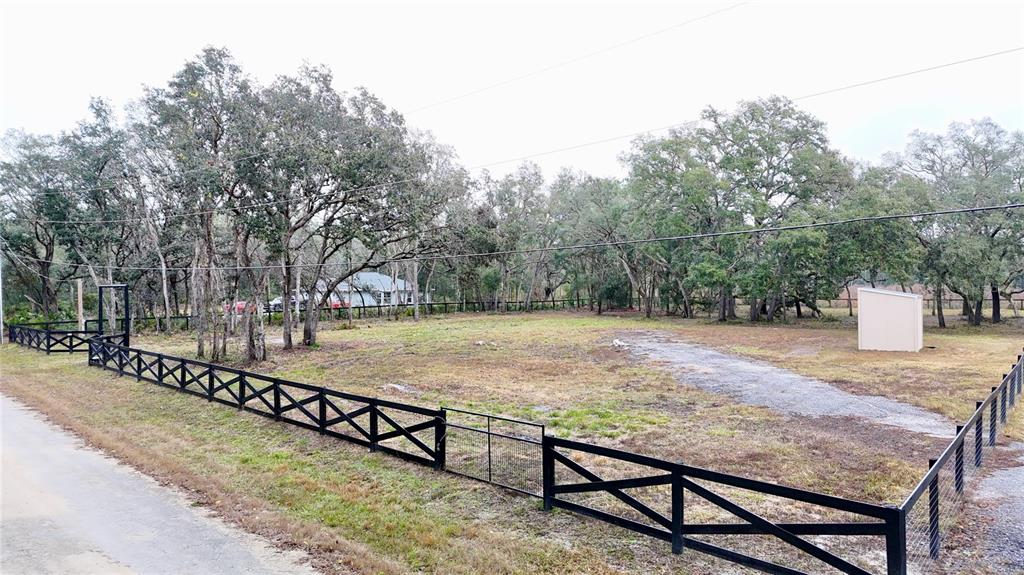 A fenced, grassy lot features mature trees and a small shed under an overcast sky — 7414 ANTIETAM DRIVE, WEBSTER, FL