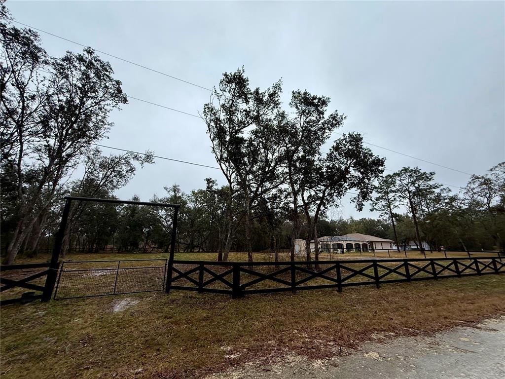 A black wooden fence and gate enclose a grassy yard with trees and a house — 7414 ANTIETAM DRIVE, WEBSTER, FL