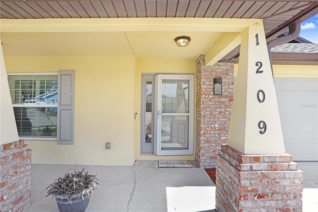 A covered front porch features a brick-based pillar with house numbers and a glass door — 1209 SPOTTED LILAC LANE, PLANT CITY, FL