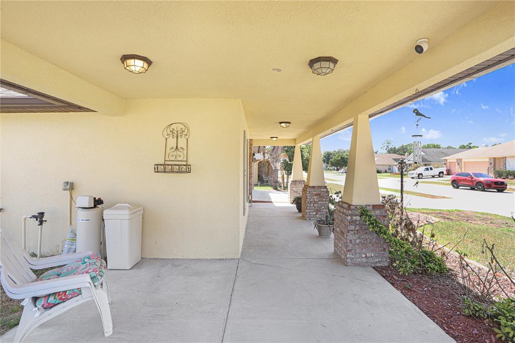 A covered concrete porch features brick-based columns, outdoor lighting, and a white water softener system — 1209 SPOTTED LILAC LANE, PLANT CITY, FL