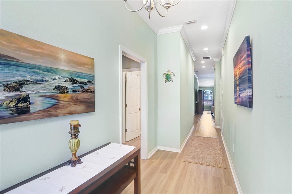 A hallway with light green walls, wood-look flooring, two landscape paintings, and a turtle wall decoration — 1209 SPOTTED LILAC LANE, PLANT CITY, FL