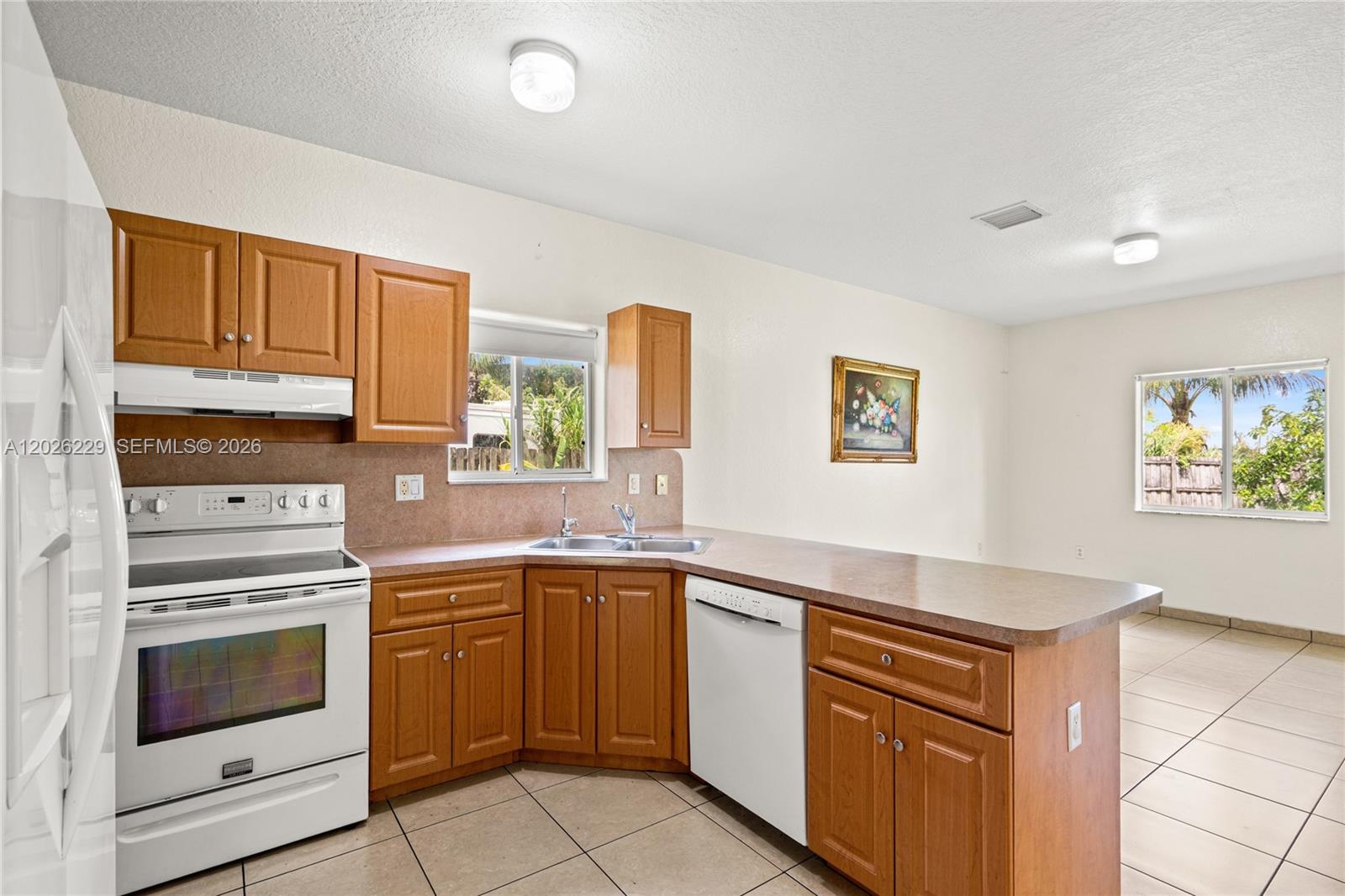 A kitchen features wood cabinets, white appliances, laminate countertops, and tile flooring — 716 SE 12th Ter, Homestead FL 33033, HOMESTEAD, FL