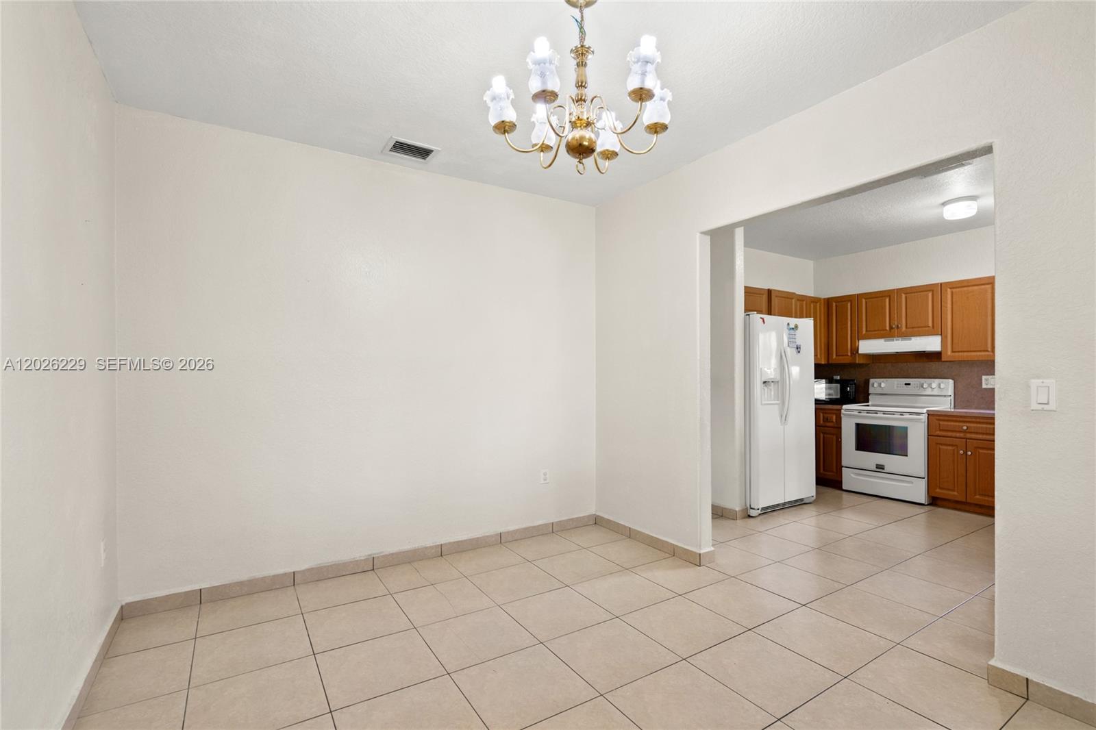 A dining area with tile flooring and a chandelier leads into a kitchen with cabinets — 716 SE 12th Ter, Homestead FL 33033, HOMESTEAD, FL