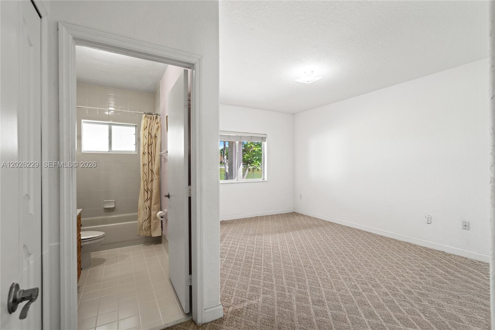 A carpeted bedroom with white walls and an adjacent bathroom with a shower-tub combo — 716 SE 12th Ter, Homestead FL 33033, HOMESTEAD, FL