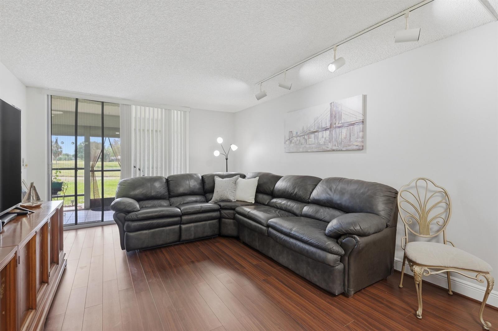 A living room features a dark leather sectional, wood flooring, and a sliding glass door — 3231 Holiday Springs Boulevard # 110, Margate FL 33063, MARGATE, FL