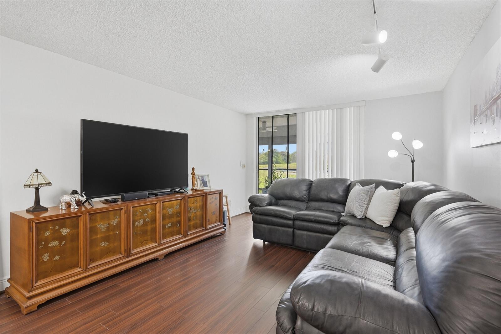 A living room features a large television on a wooden cabinet and a leather sectional — 3231 Holiday Springs Boulevard # 110, Margate FL 33063, MARGATE, FL