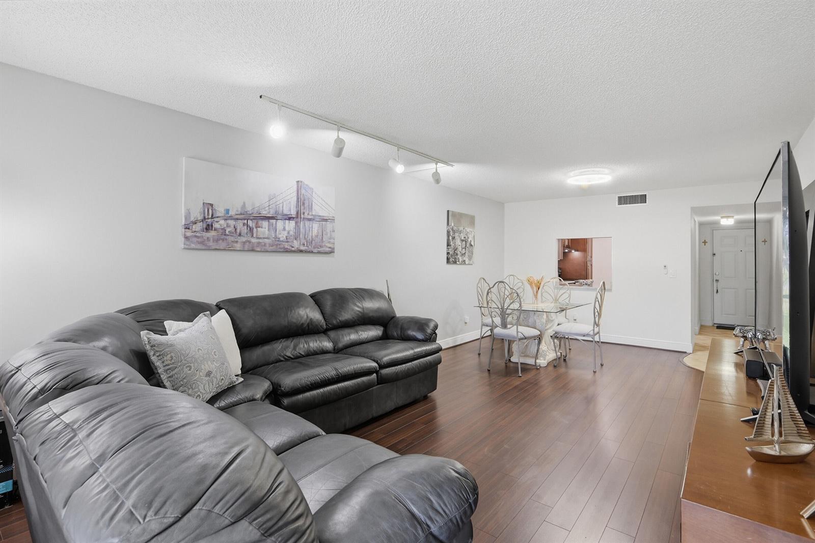 A living room with a black leather sectional, dark wood floors, and a dining area — 3231 Holiday Springs Boulevard # 110, Margate FL 33063, MARGATE, FL