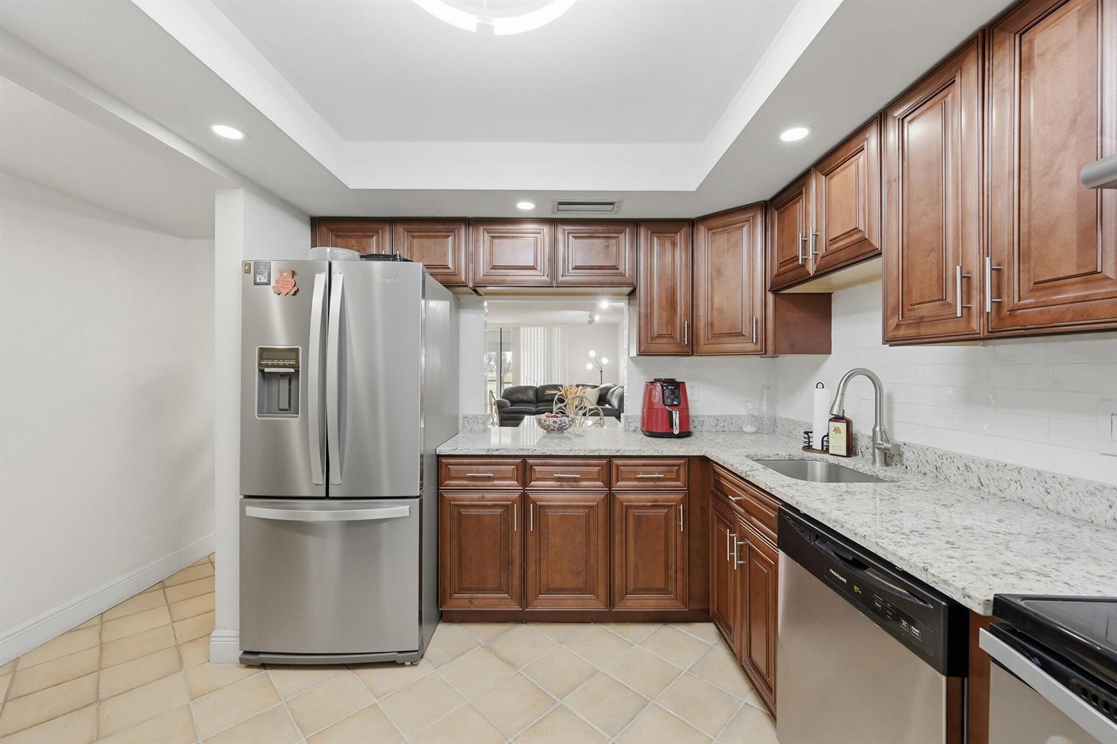 A kitchen features stainless steel appliances, wood cabinets, granite countertops, and light-colored tile flooring — 3231 Holiday Springs Boulevard # 110, Margate FL 33063, MARGATE, FL
