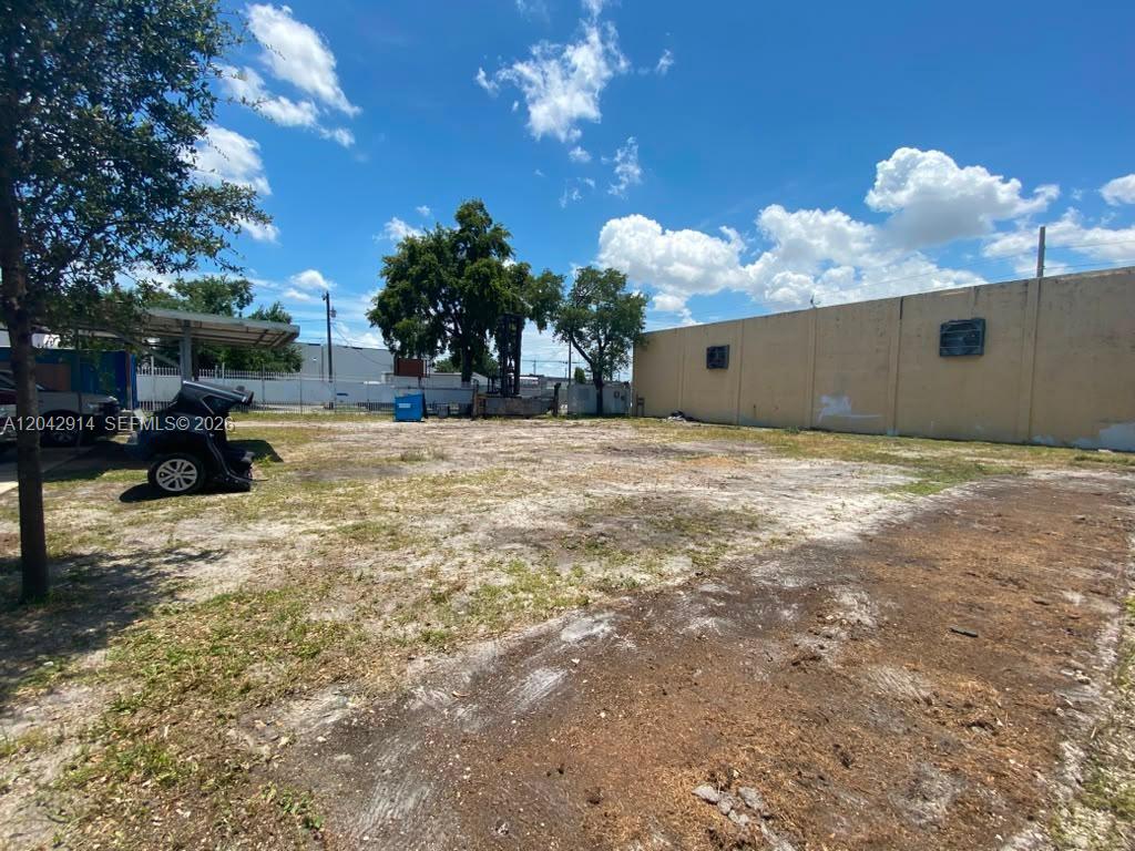 An empty, flat dirt lot sits adjacent to a tall, tan concrete wall under blue skies — 3367 NW 68th St, Miami FL 33147, MIAMI, FL