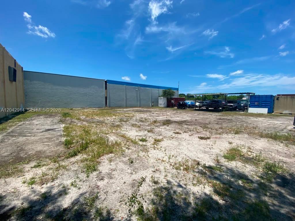 An empty dirt lot sits in front of a large industrial building under a blue sky — 3367 NW 68th St, Miami FL 33147, MIAMI, FL