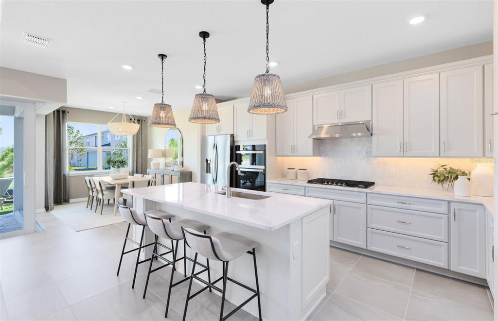 A modern kitchen features white cabinetry, a large island with bar seating, and pendant lighting — 33387 BARNEBROOK DRIVE, WESLEY CHAPEL, FL